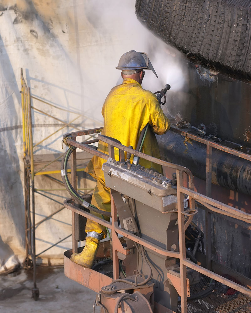 Water blasting technician in full PPE uses hydroblasting lance for industrial cleaning.