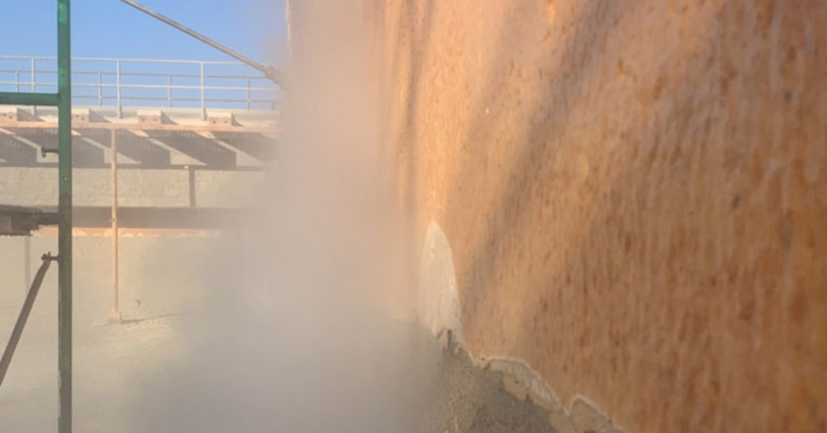 A close view of a concrete wall being pressure washed with mist covering scaffolding and exposed rough surface.