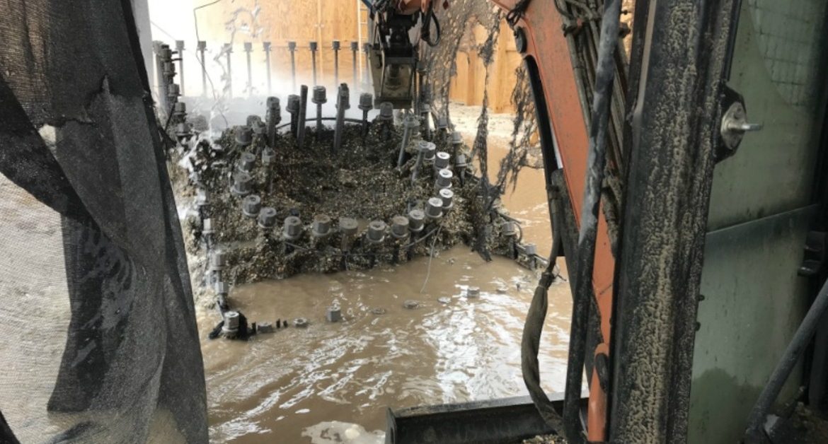 A muddy construction area with machinery, hoses, netting, and standing water around circular metal equipment.