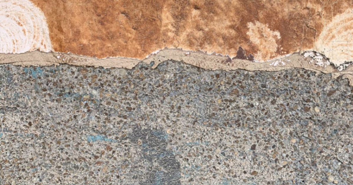 A close view of rough concrete and peeling brown surface material with exposed stones and uneven texture.